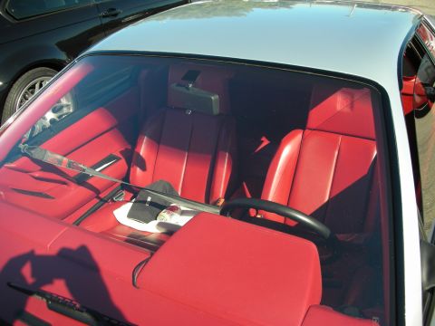 1998 Ford Crown Victoria - View through the windshield into a sports car's bright red leather interior, showing bucket seats, center console and steering wheel.