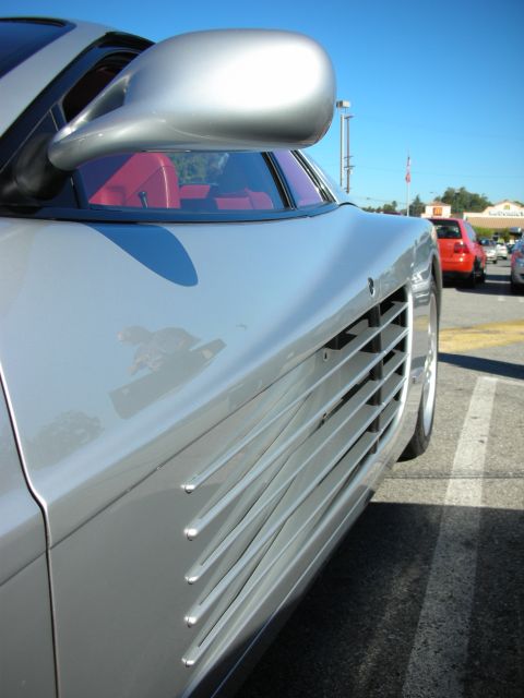 1998 Ford Crown Victoria - Close-up of a silver Ferrari's side mirror and the horizontal door strakes feeding the side air intake, with red interior visible.