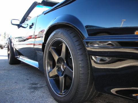 1998 Ford Crown Victoria - Low rear-quarter view of a glossy black convertible sports car riding on a black five-spoke wheel wrapped in a BFGoodrich tire.