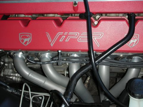 1998 Ford Crown Victoria - Close-up of a red Dodge Viper engine bay showing the ribbed valve cover stamped Viper with the snake logo above polished intake runners.