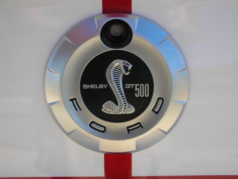 1998 Ford Crown Victoria - Round fuel-filler emblem reading Shelby GT500 Ford with a coiled cobra snake, mounted on a white car body with a red stripe.