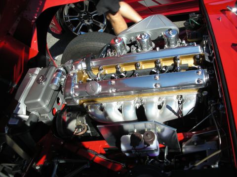 1998 Ford Crown Victoria - Polished inline-six engine with twin chrome-trimmed cam covers and gold head, mounted in the engine bay of a red classic sports car.