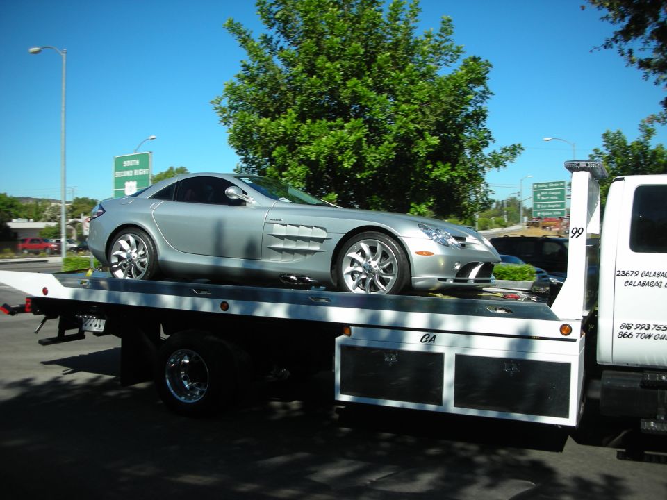 Silver Mercedes-Benz SLR McLaren loaded on a flatbed tow truck near trees