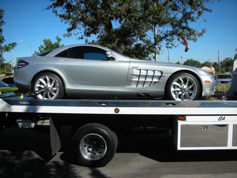 1998 Ford Crown Victoria - Silver Mercedes-Benz SLR McLaren on a flatbed truck, profile view showing the side exhaust louvers and McLaren-marked front fender.