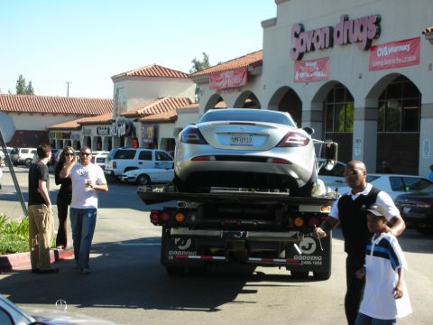 1998 Ford Crown Victoria - Rear view of a silver Mercedes-Benz SLR on a Gooding flatbed in a strip-mall parking lot, with bystanders and a Sav-on Drugs sign behind.