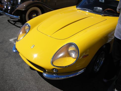 1998 Ford Crown Victoria - Front-end detail of a yellow vintage Ferrari berlinetta showing its covered headlight, chrome bumper, wire wheel and prancing-horse badge.