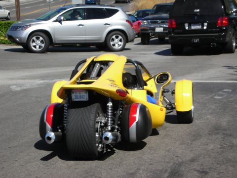 1998 Ford Crown Victoria - yellow three-wheeled reverse-trike sport vehicle parked on a street with a silver SUV and black SUVs behind it.