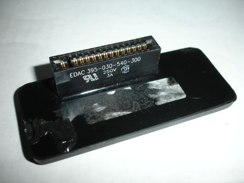 1995 Ford Taurus - A black electronic connector with visible gold pins is mounted on a black plastic housing, showing some adhesive residue and damage.