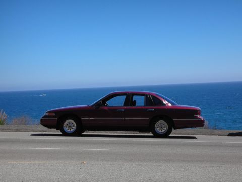 1992 Ford Crown Victoria - A maroon 1992 Ford Crown Victoria is parked on the side of a road with the ocean in the background.
