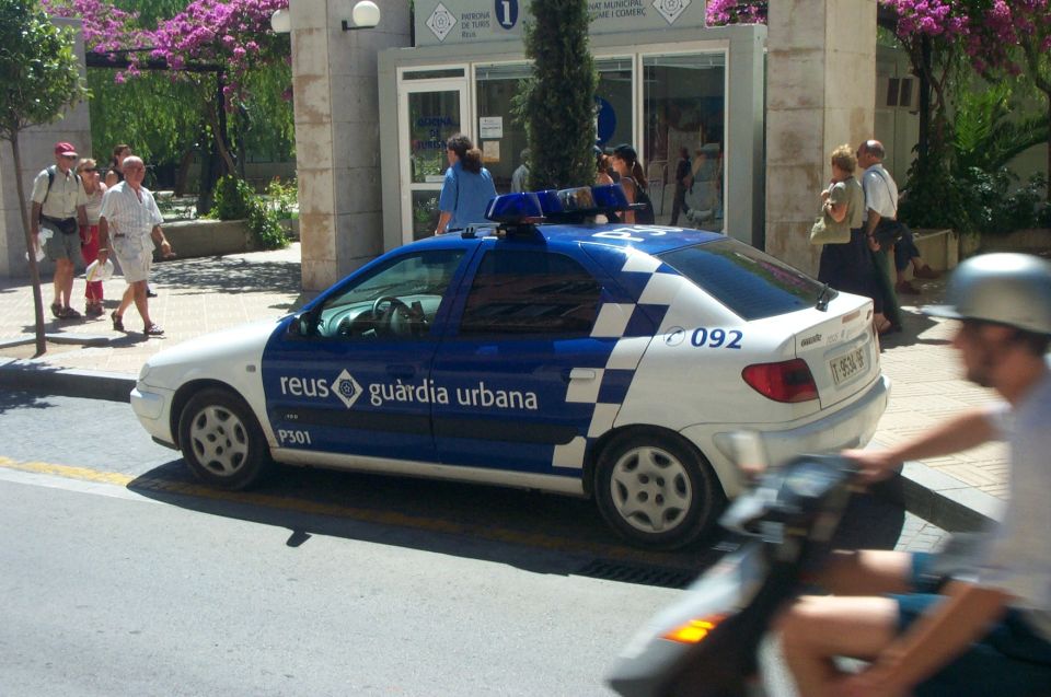 Blue and white Reus Guardia Urbana police sedan parked at a curb with pedestrians nearby