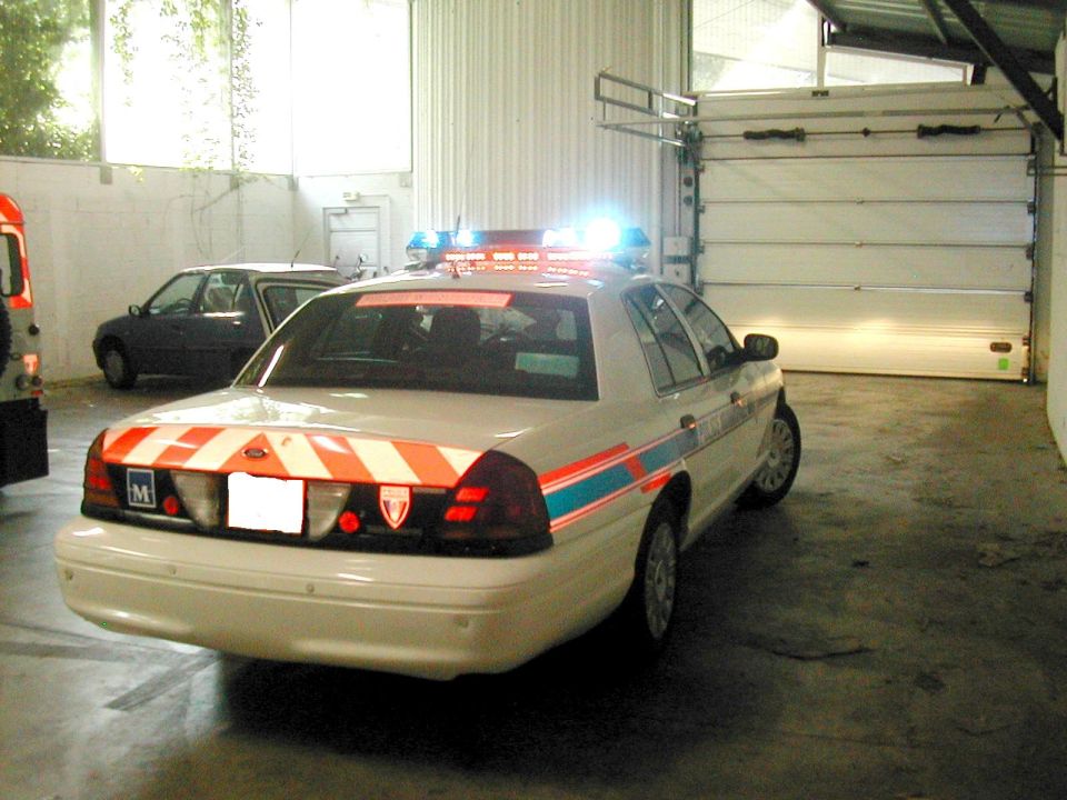 Rear of white police Crown Victoria with red chevron markings and lit blue lights
