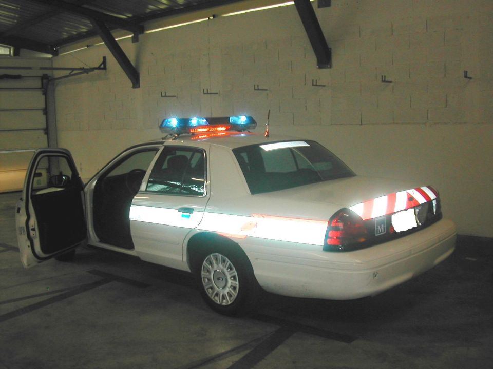 White Ford Crown Victoria police car with light bar, door open, parked in garage bay