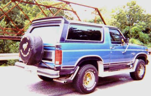 1984 Ford Bronco - A blue SUV is parked on a road with a bridge structure overhead.