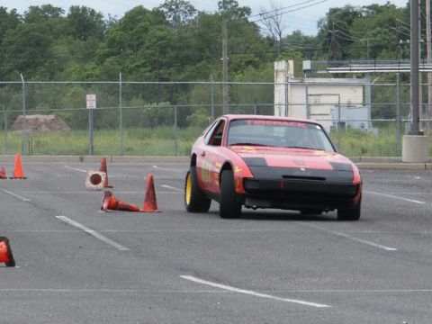 2001 Mercury Grand Marquis - A red sports car drives through a cone course on a paved lot.