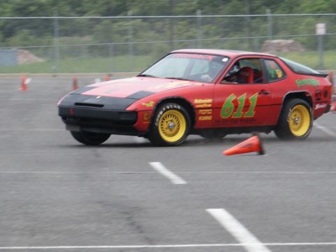 2001 Mercury Grand Marquis - A red race car with yellow wheels and the number 611 is seen on a track, navigating cones.