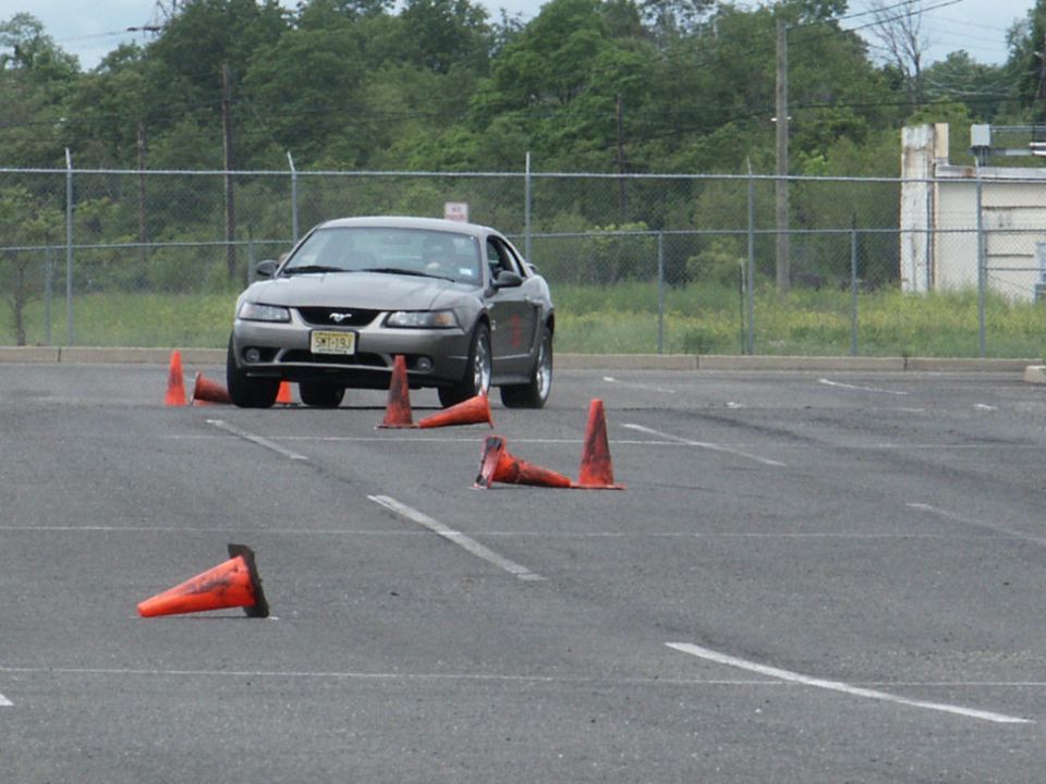 Gray Ford Mustang with a license plate starting with 'SMT' navigates an obstacle course marked by orange cones