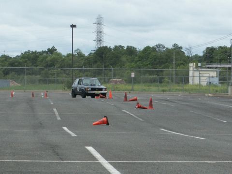 2001 Mercury Grand Marquis - A dark hatchback drives through a cone course in an empty parking lot.
