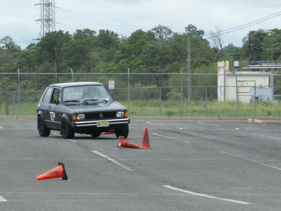 Dark gray Volkswagen Golf Mk1 with black wheels and a number 'F' on the door, navigating a cone course