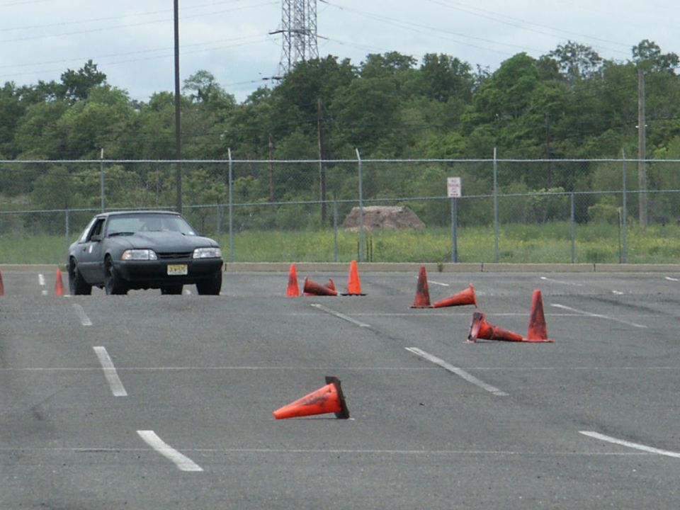 Black Ford Mustang on a paved lot with orange cones