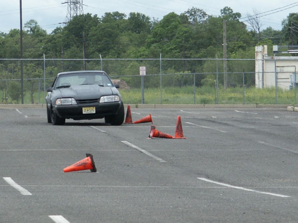 Black sedan with aftermarket hood, front view, during a cone drill