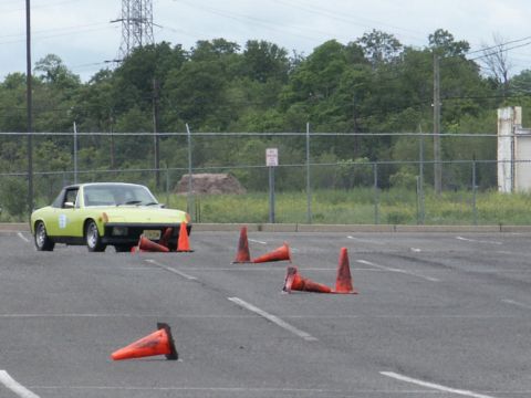 2001 Mercury Grand Marquis - A yellow sports car maneuvers through an autocross course marked by orange traffic cones on a paved lot.