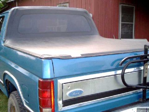 1984 Ford Bronco - This blue pickup truck features a soft tonneau cover over the bed and a Ford emblem on the tailgate.