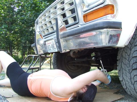 1979 Ford Bronco - A person works on the steering system of a large truck, with the front grille and bumper visible.