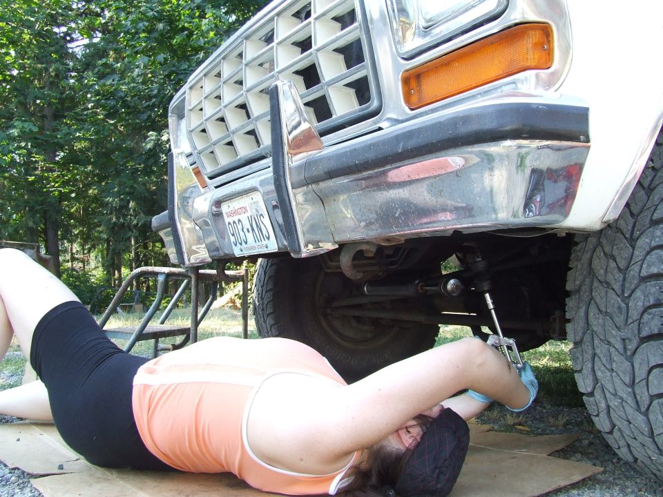 Person under the front of a white Ford Bronco using a grease gun on the front end