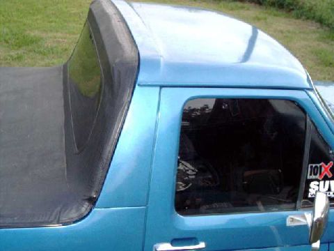 1984 Ford Bronco - A blue pickup truck is shown from the side, a black soft top covering the bed and a sticker on the window.