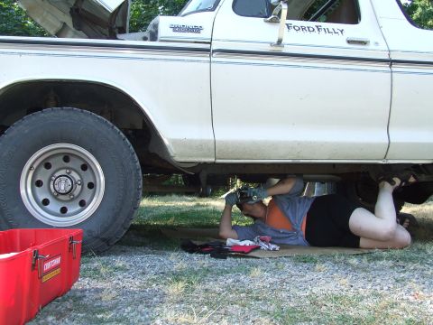 1979 Ford Bronco - A person lies on the ground performing maintenance on the underside of a Ford Bronco.