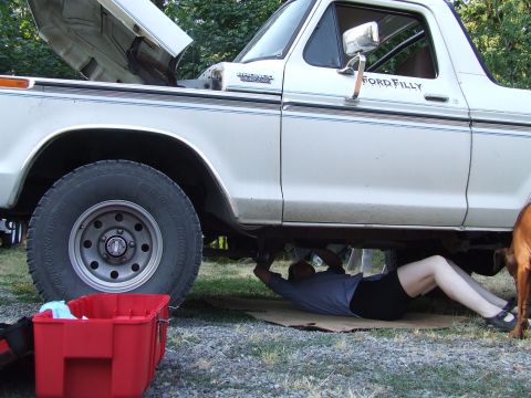 1979 Ford Bronco - Person working on the underside of a white 1979 Ford Bronco, hood is open.
