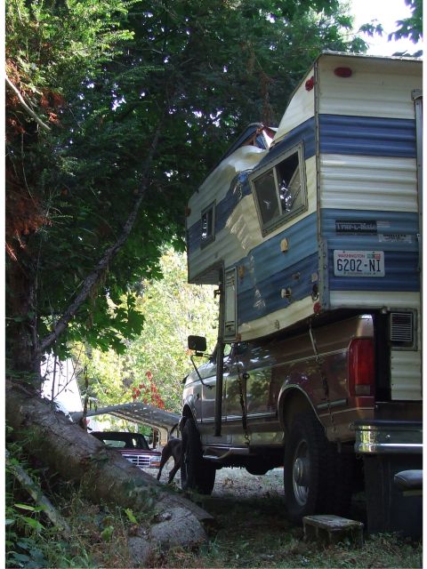1996 Ford Bronco - A truck with a camper shell is parked outdoors, with another vehicle visible in the background.