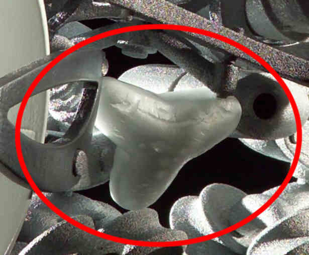 Close-up of a metal engine component with a red circle highlighting a light-colored part