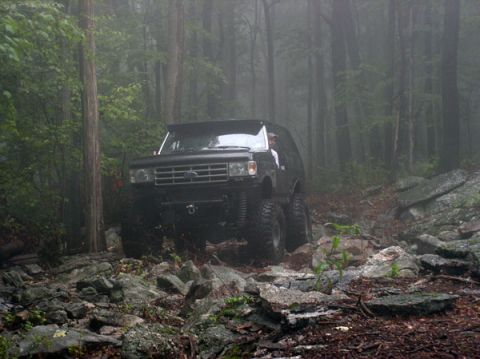 1988 Ford Bronco - This modified SUV navigates a challenging, rocky path through a misty wooded area.
