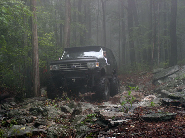 Black off-road SUV driving over rocks in a foggy forest. Driver visible