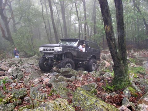 1988 Ford Bronco - Modified Ford Bronco navigates a challenging rocky trail in a wooded area.