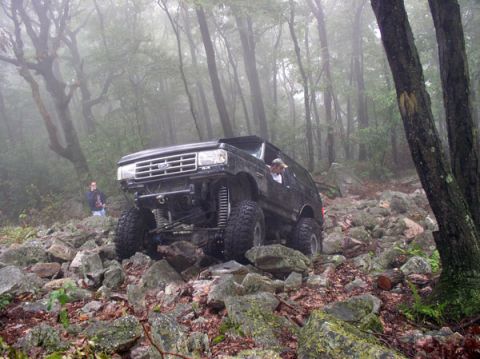 1988 Ford Bronco - A modified Ford Bronco navigates a rocky trail in a misty wooded area.