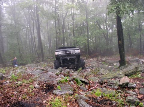 1988 Ford Bronco - A modified black 1989 Ford Bronco tackles a challenging rocky terrain in a misty forest setting.