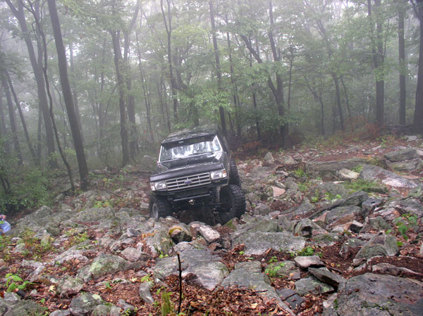 Lifted black Ford 4x4 descending a wet rocky trail in foggy woods