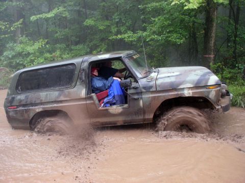 1988 Ford Bronco - A camouflaged Ford Bronco navigates a muddy off-road course.