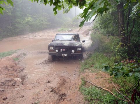 1988 Ford Bronco - Off-road vehicle navigates a challenging muddy path on a wooded trail.