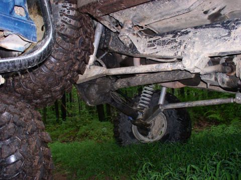 1988 Ford Bronco - The undercarriage of a heavily modified off-road vehicle is shown, with large tires and suspension components visible.