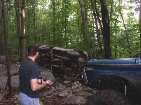 1988 Ford Bronco - A man observes an overturned vehicle and a blue truck in a rocky, wooded environment.
