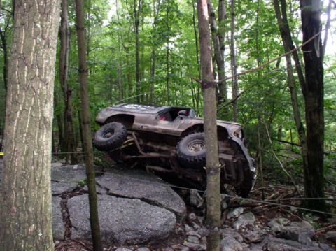 1988 Ford Bronco - An off-road SUV is precariously tilted on large rocks amidst a dense forest environment.