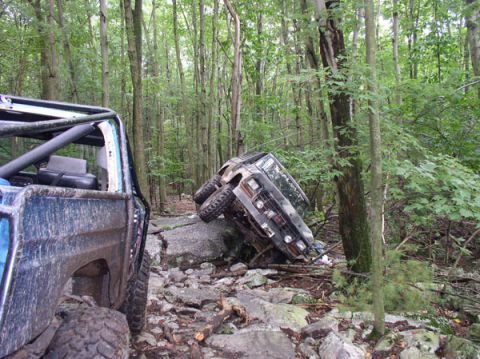 1988 Ford Bronco - Two off-road vehicles navigate a rocky trail in a wooded area.