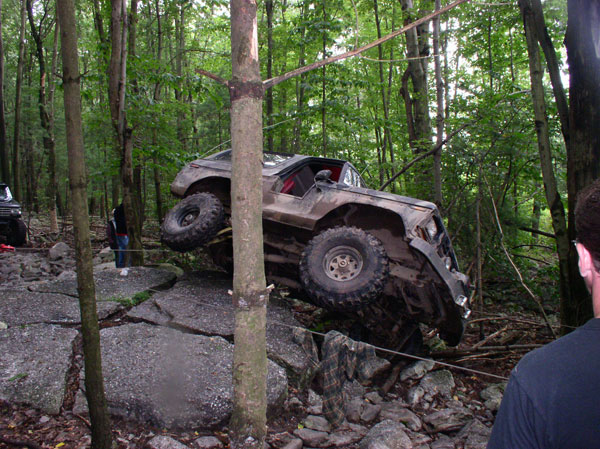 Brown off-road vehicle tilted on rocks, front right wheel off ground