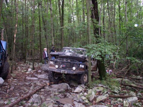 1988 Ford Bronco - Three-quarter front view of a lifted topless Ford Bronco with its hood removed, headlights on, winch-equipped front bumper and mud-terrain…