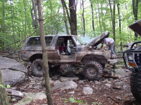 1988 Ford Bronco - A muddy 1988 Ford Bronco is being serviced off-road, with its hood open and another vehicle visible to the right.
