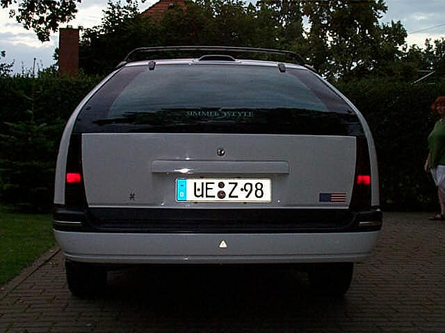 Rear of white station wagon with German UE Z-98 plate on brick driveway at dusk