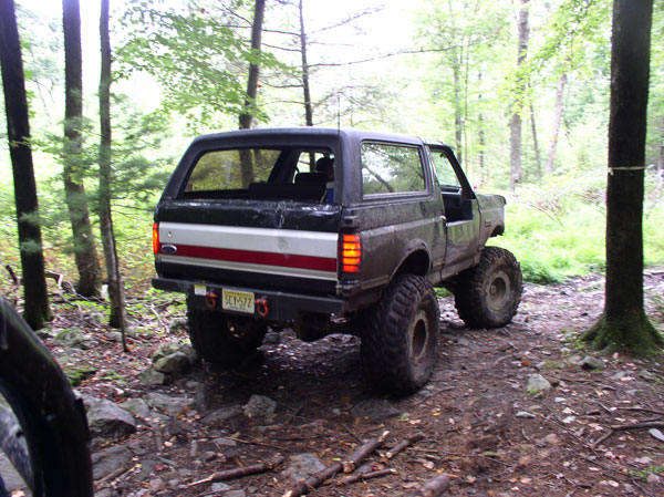 Black 1988 Ford Bronco with off-road tires on a wooded trail